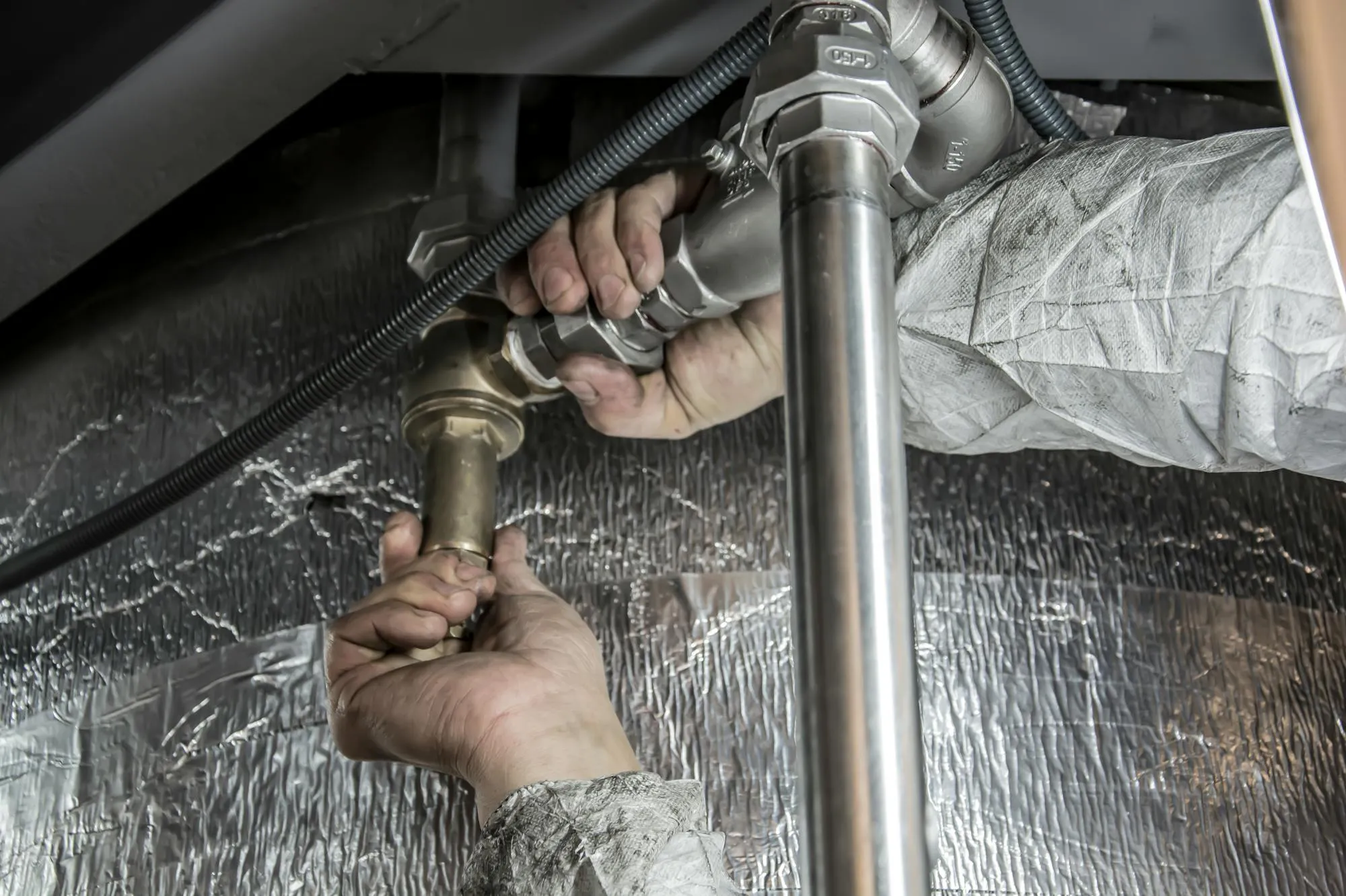 Plumber tightening a brass fitting under a sink